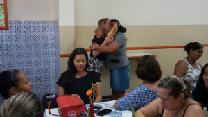 FOTO: A foto mostra a presidenta Sra. Heliana Guimarães Diniz  entregando um presente a uma colaboradora, as duas estão se abraçando. 