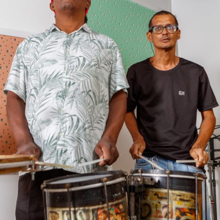 foto dois alunos em uma sala do Centro Musical Imaginasom no ICB. Eles estão em pé, um ao lado do outro tocando instrumento de percussão com baquetas.