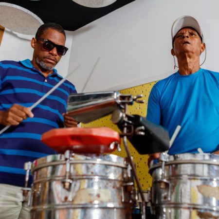 foto dois alunos em uma sala do Centro Musical Imaginasom no ICB. Eles estão em pé, um ao lado do outro tocando instrumento de percussão com baquetas.