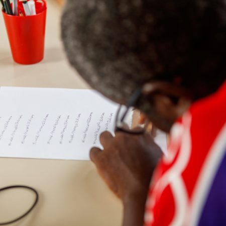 foto de um homem, na altura do ombro, com foco nele segurando um papel e uma caneta sobre uma mesa, treinando a assinatura de seu nome.